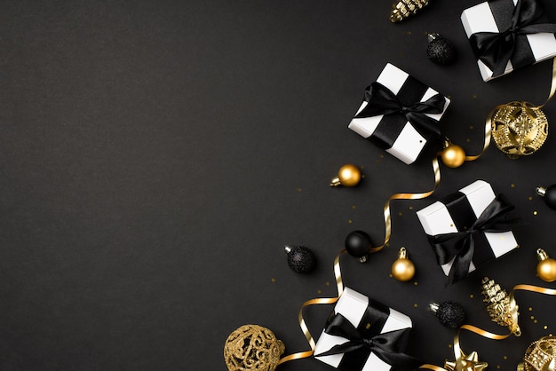 Top view photo of christmas decorations gold and black balls toy cones white gift boxes with black ribbon bows serpentine and sequins on isolated black background with blank space