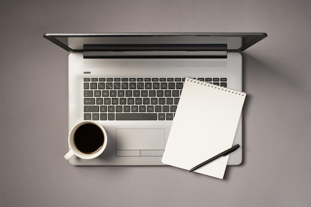 Top view photo of cup of drink pen and reminder on grey laptop on isolated grey background with blank space