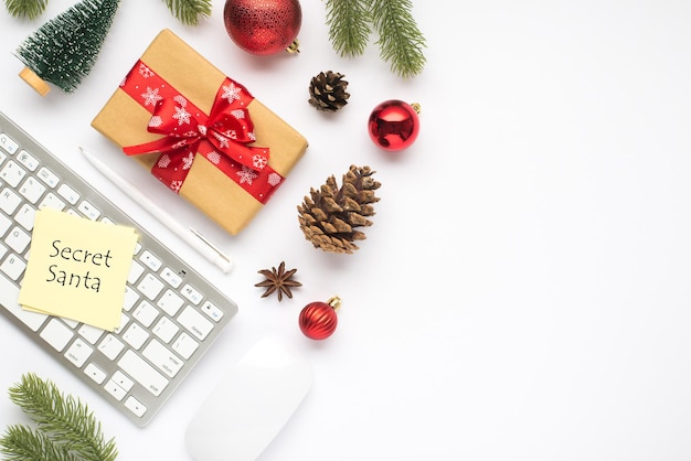 Foto vista dall'alto di confezione regalo con fiocco rosso adesivo carta per appunti sulla tastiera computer mouse penna albero di natale rosso palle abete ramoscelli di pino pigne e anice su sfondo bianco isolato con copyspace