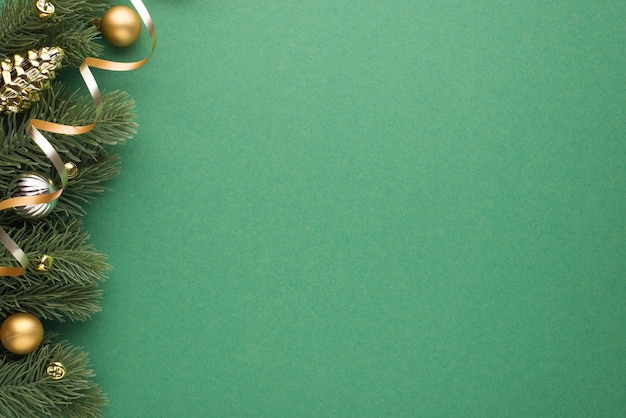 Top view photo of gold and silver christmas tree balls toy cone small bells and serpentine on pine twigs on isolated green background with copyspace