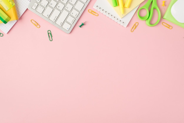 Top view photo of green and yellow stationery organizers pens clips pushpins scissors ruler stickers eraser keyboard and mouse on isolated pastel pink background with copyspace