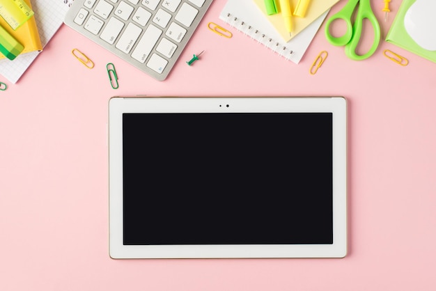 Top view photo of green and yellow stationery organizers pens clips pushpins scissors ruler stickers eraser keyboard mouse and tablet computer on isolated pastel pink background with blank space