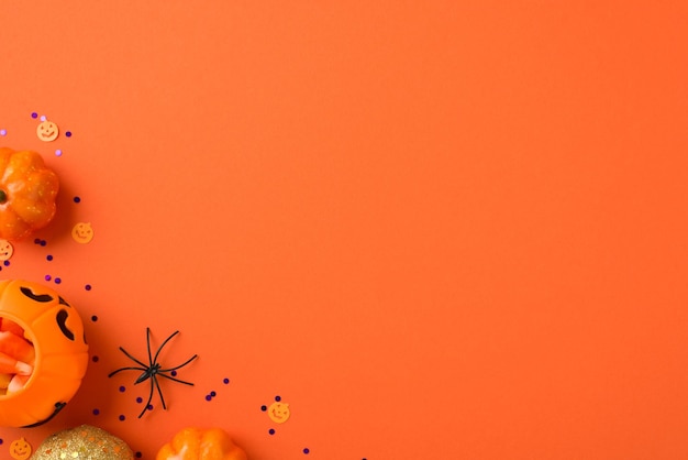 Top view photo of halloween decorations pumpkin basket with candy corn spider orange and golden small pumpkins and violet sequins on isolated orange background with copyspace