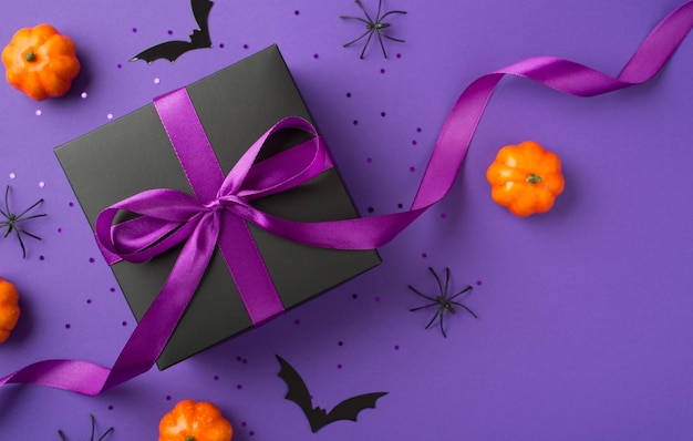 할로윈 장식 호박 박쥐 거미 검은 선물 상자, 보라색 리본 활과 카피스페이스가 있는 격리된 보라색 배경에 스팽글이 있는 상위 뷰 사진