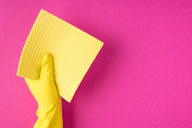 Top view photo of hand in yellow glove holding yellow viscose rag on isolated pink background with blank space