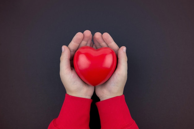 Top view photo of hands holding red heart on black background healthcare love organ donation mindfulness wellbeing family insurance and CSR concept World Heart Day