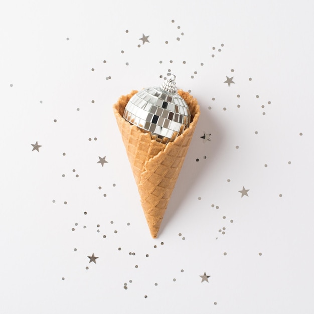 Top view photo of ice cream cone with christmas tree disco ball and silver confetti on isolated white background