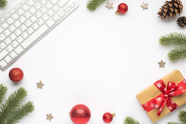 Top view photo of keyboard christmas tree balls pine twigs cones shiny stars and giftbox with red bow on isolated white background with empty space in the middle