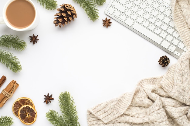 Top view photo of keyboard cup of hot drinking pine twigs cones anise cinnamon sticks dried lemon slices and sweater on isolated white background with empty space in the middle