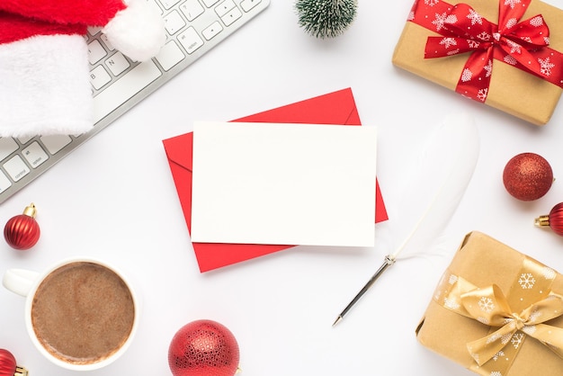 Top view photo of keyboard cup of hot drinking santa claus hat pine toy red christmas tree balls gift boxes with ribbon bows red envelope card and quill on isolated white background with blank space