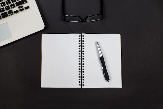 Top view photo of laptop with notepad pen and glasses on isolated black background copy space place for text