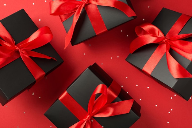 Top view photo of levitating black gift boxes with red ribbon bow and sequins on isolated red background