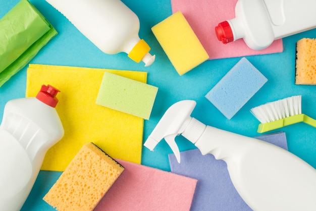 Top view photo of multicolor sponges viscose rags garbage bags brush and detergent bottles without label on isolated pastel blue background with copyspace