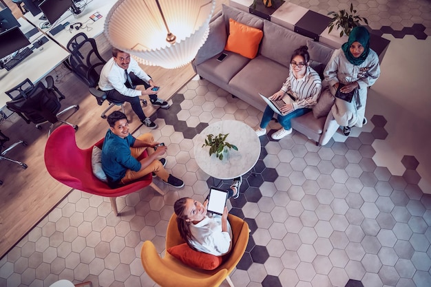 Top view photo of Multiethnic startup business team having brainstorming in relaxation area of modern office interior working on laptop and tablet computer. High-quality photo