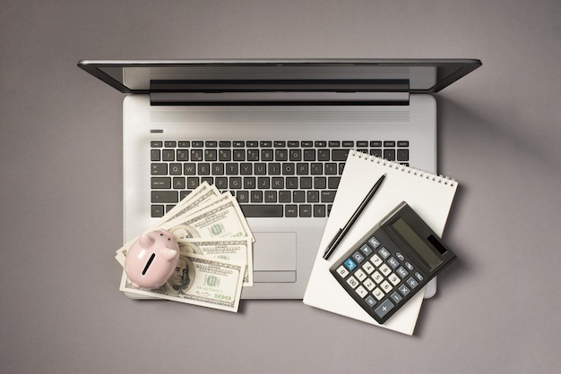 写真 孤立した灰色の背景に開いた灰色のラップトップのお金のドルの計算機のペンとコピーブックのファンの貯金箱の上面写真