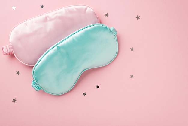 写真 空のスペースで分離されたパステル ピンクの背景に 2 つのライト ピンクとブルーのシルクの睡眠マスクと星形の紙吹雪の上から見た写真
