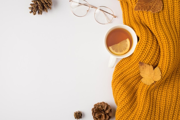 Фото Фотография сверху желтого вязаного шарфа, чашки чая с лимонно-желтыми осенними листьями шелковицы, сосновыми шишками и стильными очками на изолированном белом фоне с копирайтом