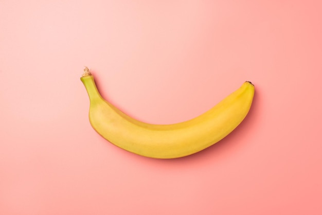 Top view photo of one unpeeled yellow banana in the middle on isolated pastel pink background with blank space