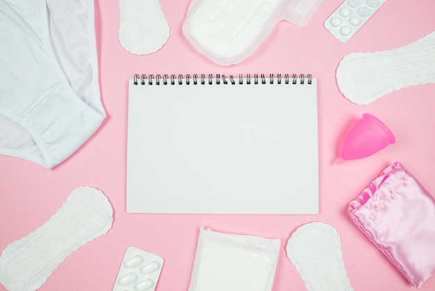 Top view photo of open planner over sanitary napkins linen and pills on isolated pastel pink background with empty space