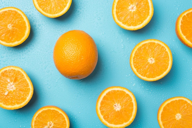 Top view photo of orange slices and one whole orange water\
drops on isolated light blue background