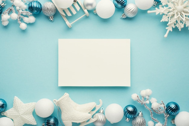 Top view photo of paper sheet white blue and silver christmas tree decorations snowflake star balls ice skates sled and snowy branches on isolated pastel blue background with blank space