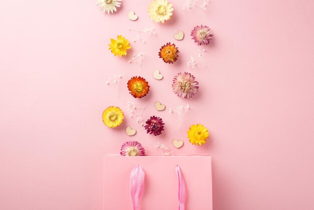 Foto vista dall'alto della borsa rosa della spesa di carta molti fiori colorati con rami di gypsophila e coriandoli a forma di cuori sparsi sopra la borsa sullo sfondo vuoto isolato rosa pastello