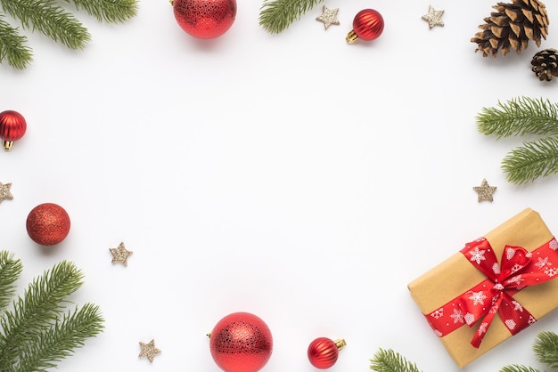 Top view photo of pine branches red christmas tree balls cones stars and gift box with red bow on isolated white background with blank space in the middle