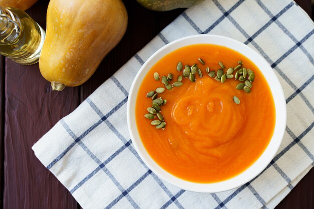 Top view photo of pureed pumpkin soup in a white bowl on dark table