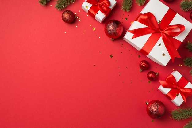 빨간 크리스마스 트리 볼 소나무 가지 흰색 선물 상자, 리본 활과 황금 색종이 조각이 카피스페이스가 있는 격리된 빨간색 배경에 있는 상위 뷰 사진