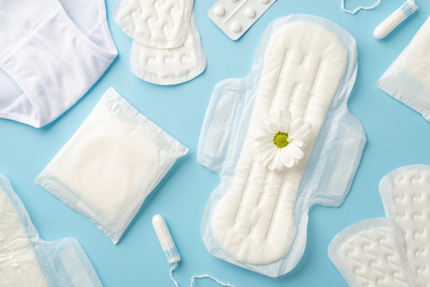 top view photo of sanitary napkins camomile flower bud tampons lingerie and painkiller pills on isolated pastel blue background