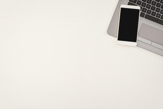空白のスペースと孤立した白い木製のテーブルの背景にラップトップ上のスマートフォンの上面写真