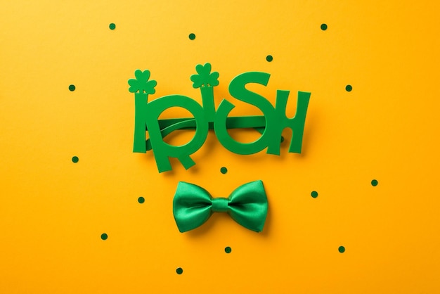 Top view photo of st patrick's day decorations funny outfit irish party glasses and green bowtie on isolated yellow background