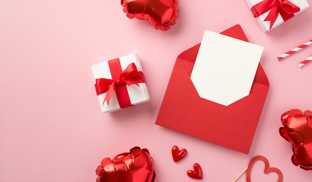 Вид сверху фото украшений на день святого валентина, открытый красный конверт с бумажным листом, маленькие сердечки, подарочные коробки, соломинки и воздушные шары в форме сердца на изолированном пастельно-розовом фоне с пустым пространством