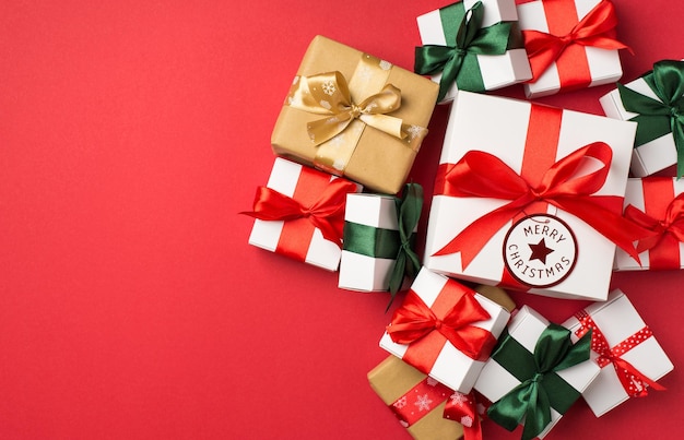 Top view photo of stack of white gift boxes with ribbon bows and tag with inscription merry christmas on isolated red background with empty space