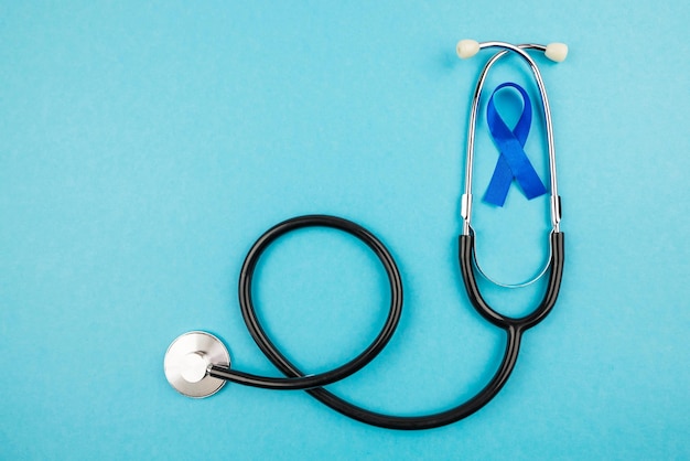 Top view photo of stethoscope and blue ribbon symbol of prostate cancer awareness on isolated pastel blue background with copyspace