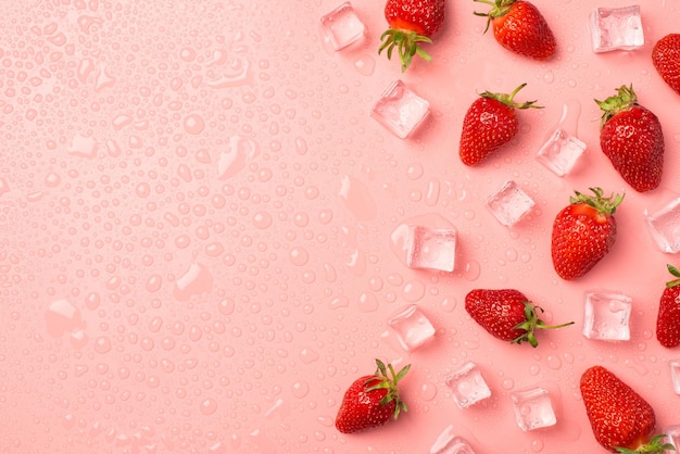 Foto dall'alto di fragole a cubetti di ghiaccio a destra e gocce d'acqua su sfondo rosa pastello isolato con spazio vuoto a sinistra