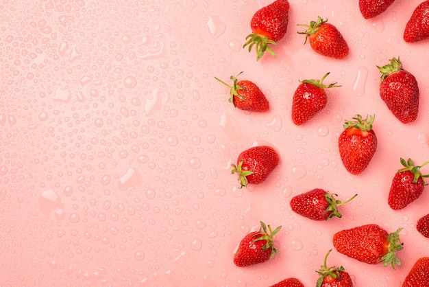 Top view photo of strawberries and water drops on the right on isolated pastel pink background with copyspace on the left