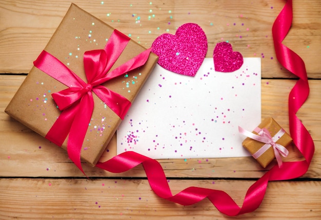 Top view photo of Valentine's day decor gift box, paper heart, sequins, a sheet of paper on a wooden background.