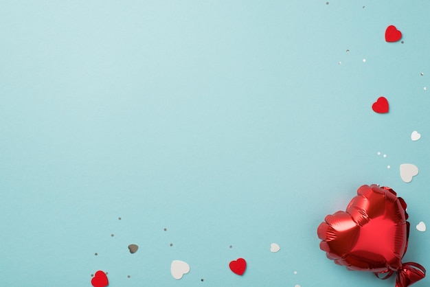 Top view photo of valentine's day decorations heart shaped balloon red and white hearts confetti and sequins on isolated pastel blue background with copyspace