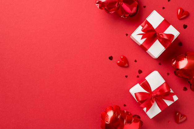 Top view photo of valentine's day decorations white gift boxes with red ribbon bows heart shaped balloons small hearts and confetti on isolated red background with empty space