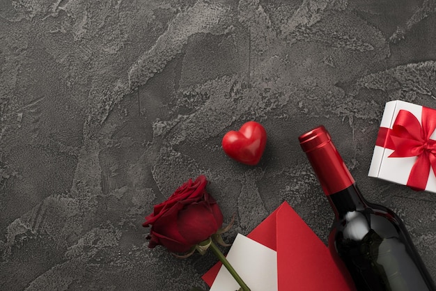 Top view photo of valentine's day decorations wine bottle white giftbox with red bow heart envelope with letter and red rose on isolated textured dark grey concrete background with copyspace