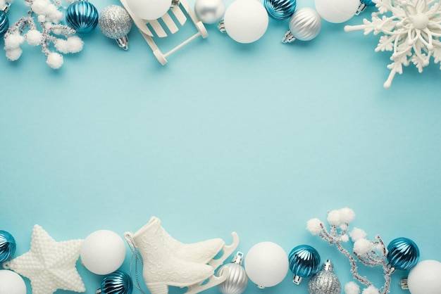 Top view photo of white blue and silver christmas tree decorations snowflake star balls ice skates sleigh and snowy twigs on isolated pastel blue background with empty space