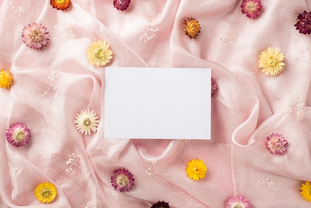 Top view photo of the white card in the middle and many different colorful nice flowers scattered on the pastel pink textile background