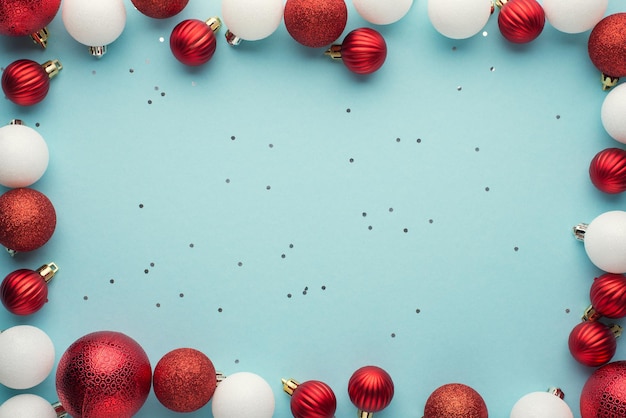 Top view photo of white and red christmas tree balls and sequins on isolated pastel blue background with empty space in the middle