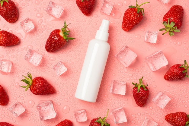 Top view photo of white spray bottle without label in the middle strawberries ice cubes and drops on isolated pastel pink background with copyspace