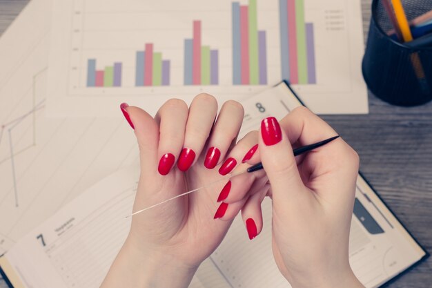 Photo top view photo of woman's hand holding nail fail against opened diary and graphs on background