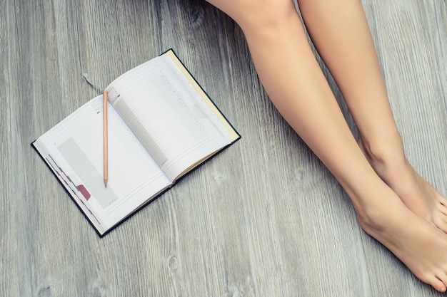 Top view photo of womans legs on wooden floor with opened diary