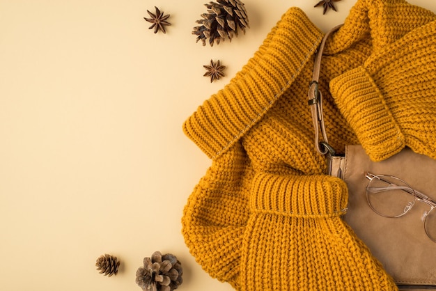 Вид сверху фото желтого свитера, кожаной сумочки, стильных очков, аниса и сосновых шишек на изолированном пастельно-бежевом фоне с копирайтом