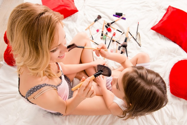 Top view photo of young woman and her little child doing makeup