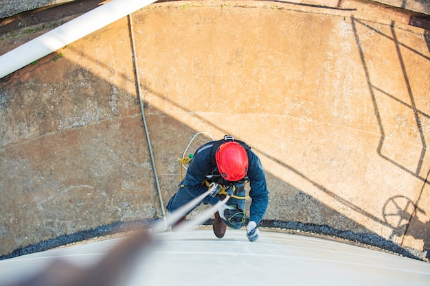 Top view pic of industrial rope access welder working at height
wearing harness, helmet safety equipment rope access inspection of
thickness storage tank industry.